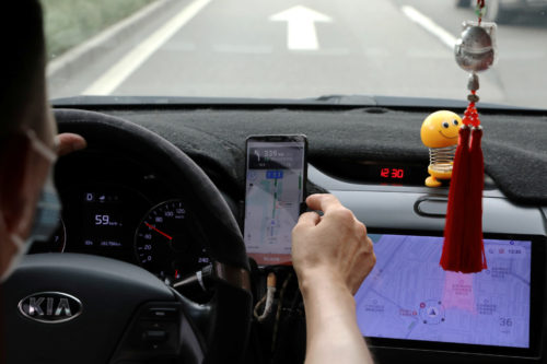 A driver of Chinese ride-hailing service Didi drives with a phone showing a navigation map on Didi's app, in Beijing, China